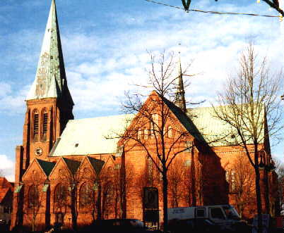 Eine Backsteinkirche, braun; links der Turm der Kirche; etwa in der Bildmitte das Querschiff