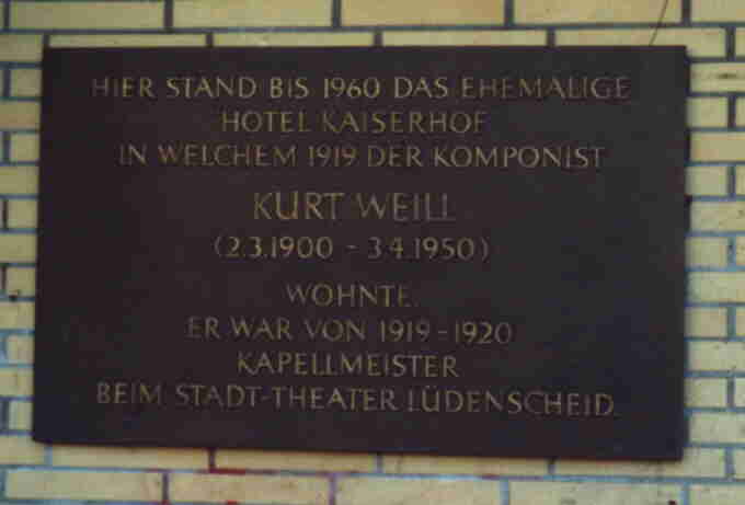 Eine Tafel. Der Text: 'Hier stand bis 1960 das ehemalige Hotel Kaiserhof in welchem 1919 der Komponist Kurt Weil (2.3.1900 - 3.4.1950) wohnte. Er war von 1919 - 1920 Kapellmeister beim Stadt-Theater Lüdenscheid...