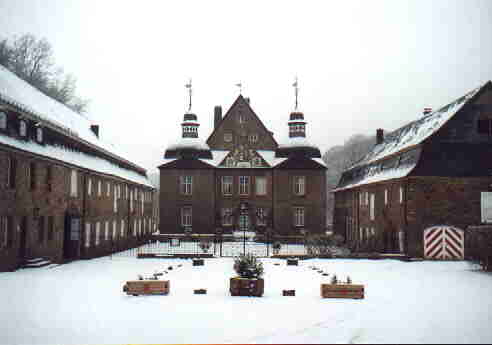 In der Bildmitte das Hauptgebäude des Schloßes, links und recht, angebaut zwei Türme, vor dem Hauptgebäde das eiserne Schloßtor, die Nebengebäde rechts und links der Bildmitte.