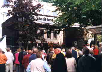 Eine überdachte Bühne, darüber ein Transparent mit der Aufschrift 'Stadtfest'. Menschen sind  auf und vor der Bühne...